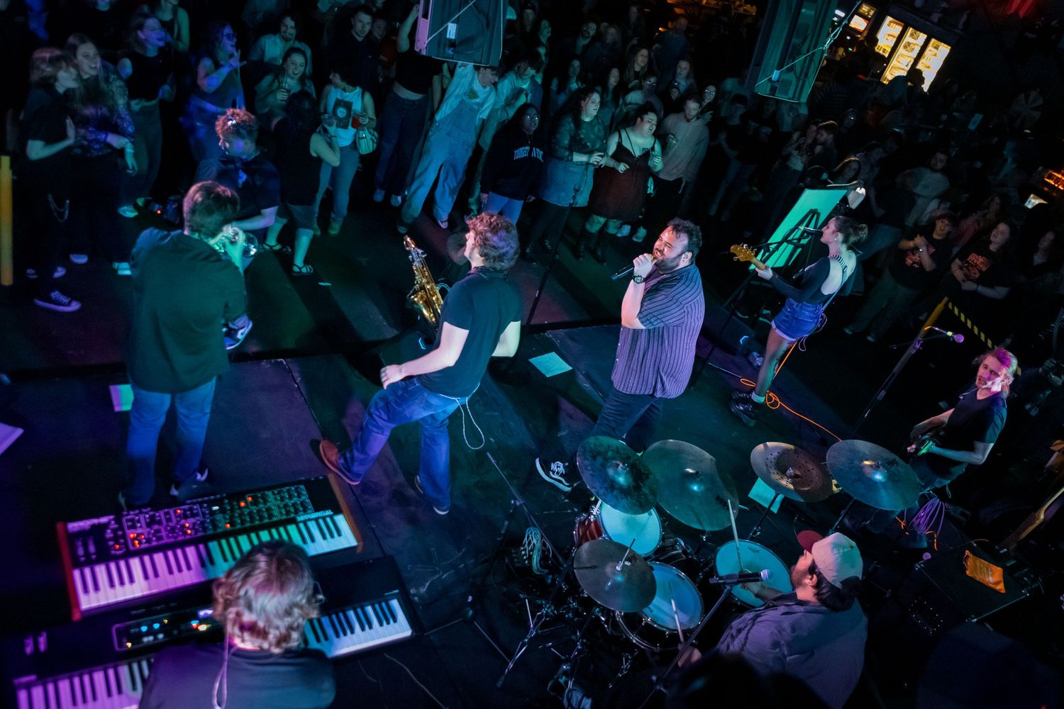 Wide shot of concert venue with crowd and performers under purple lighting.