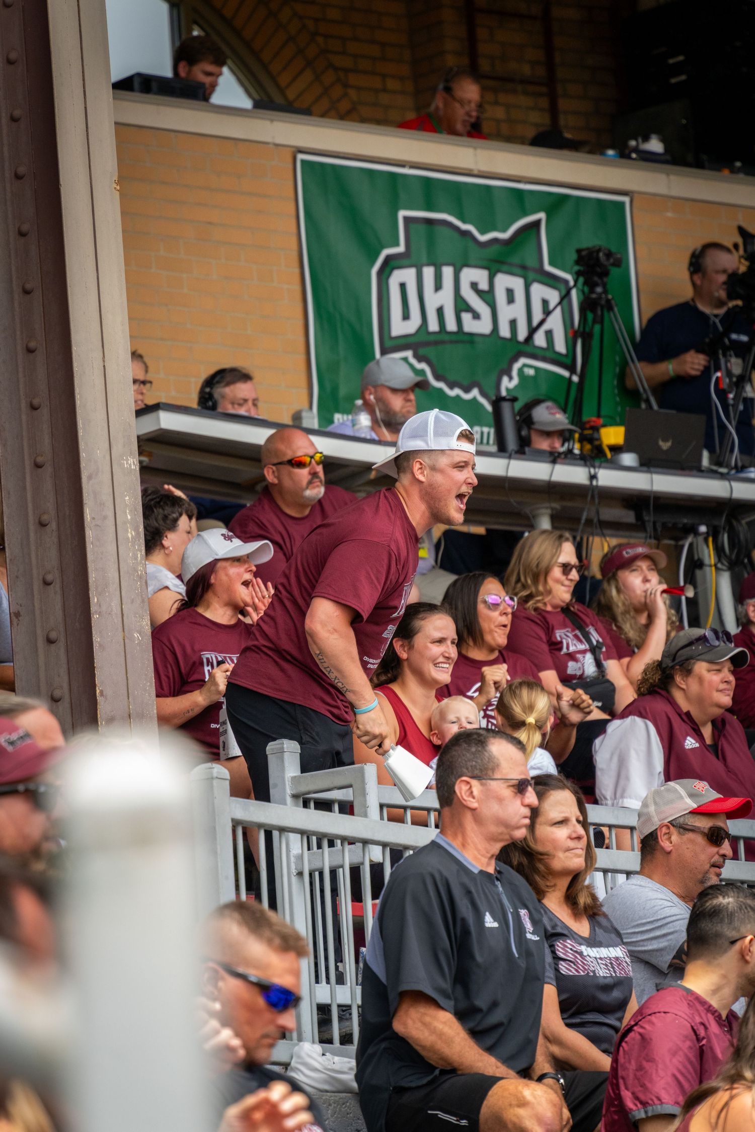 Crowd of spectators in maroon attire watching from stadium bleachers.