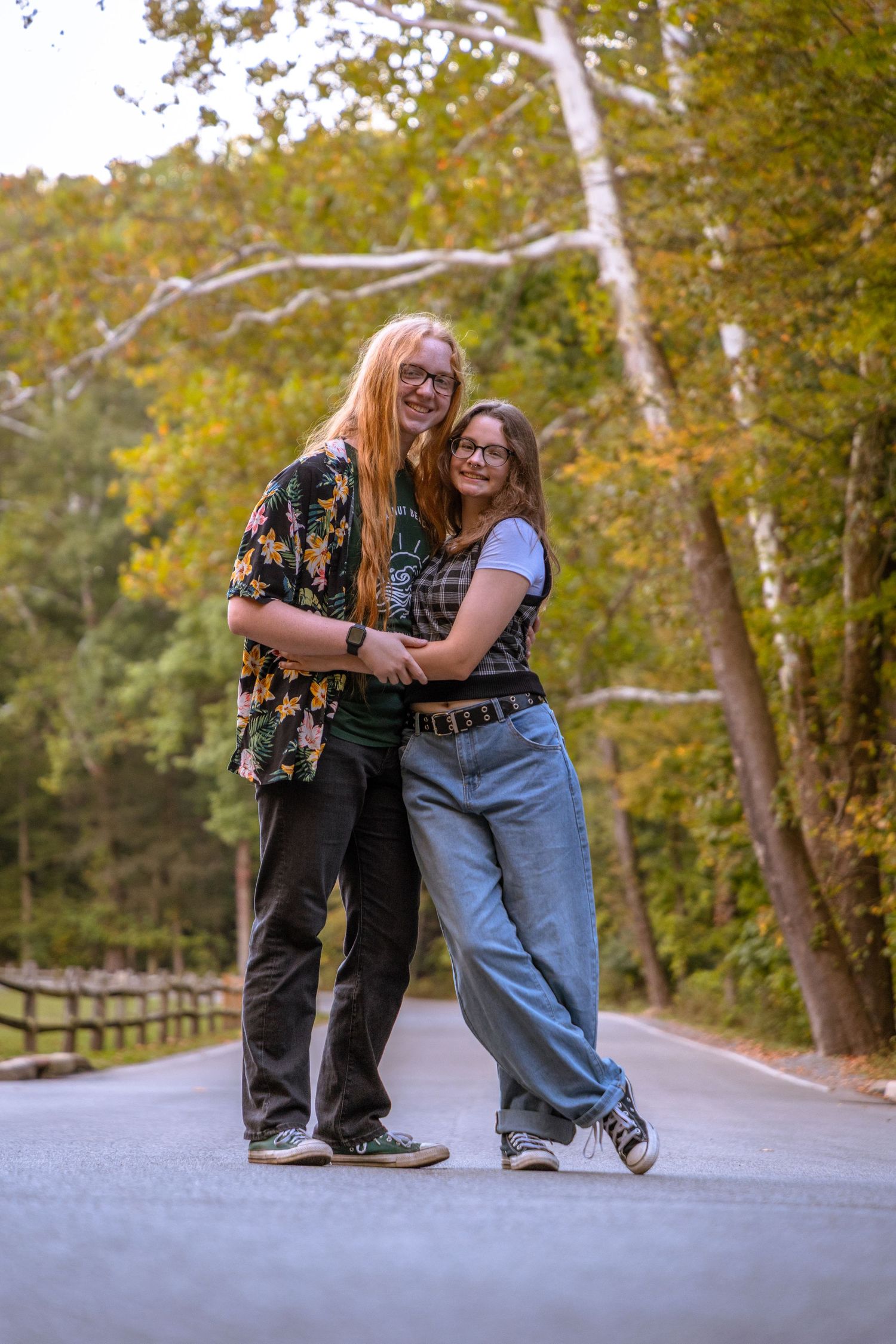 Two people playfully interact on a tree-lined path during autumn.
