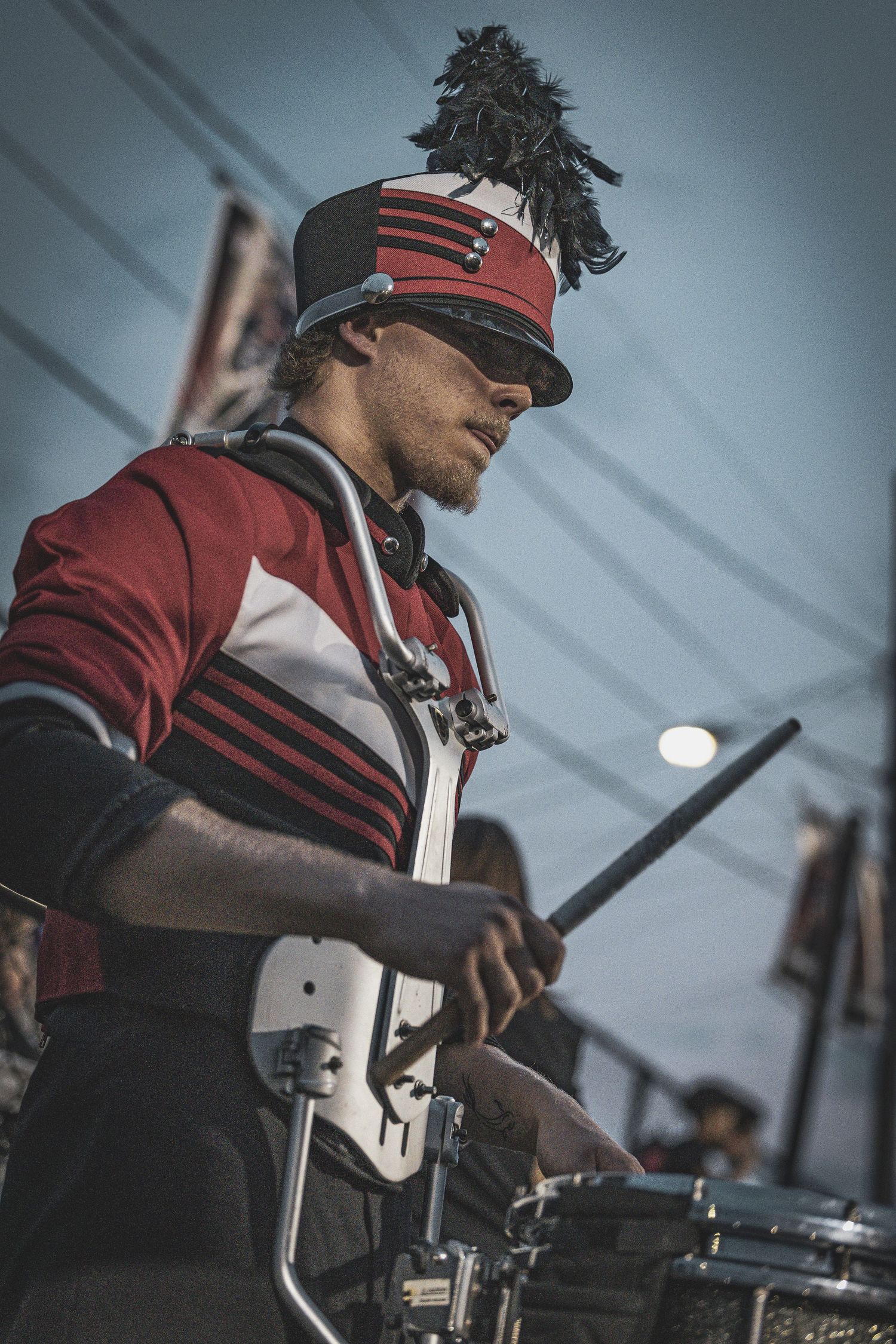 A marching band member in red uniform plays drums during a performance.