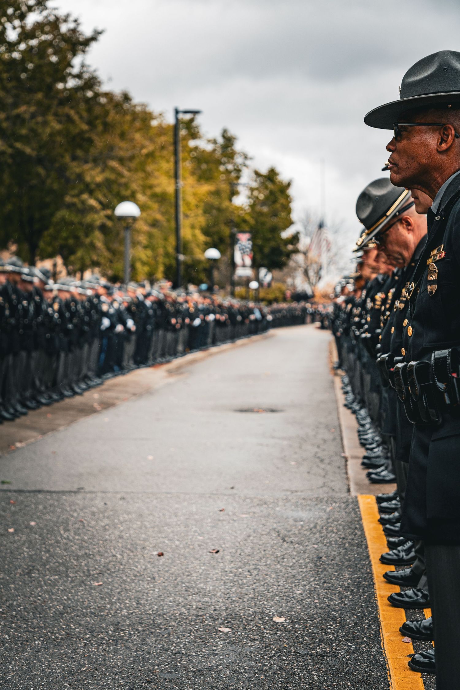 Officers in formal attire line both sides of a wet pathway during a ceremony.