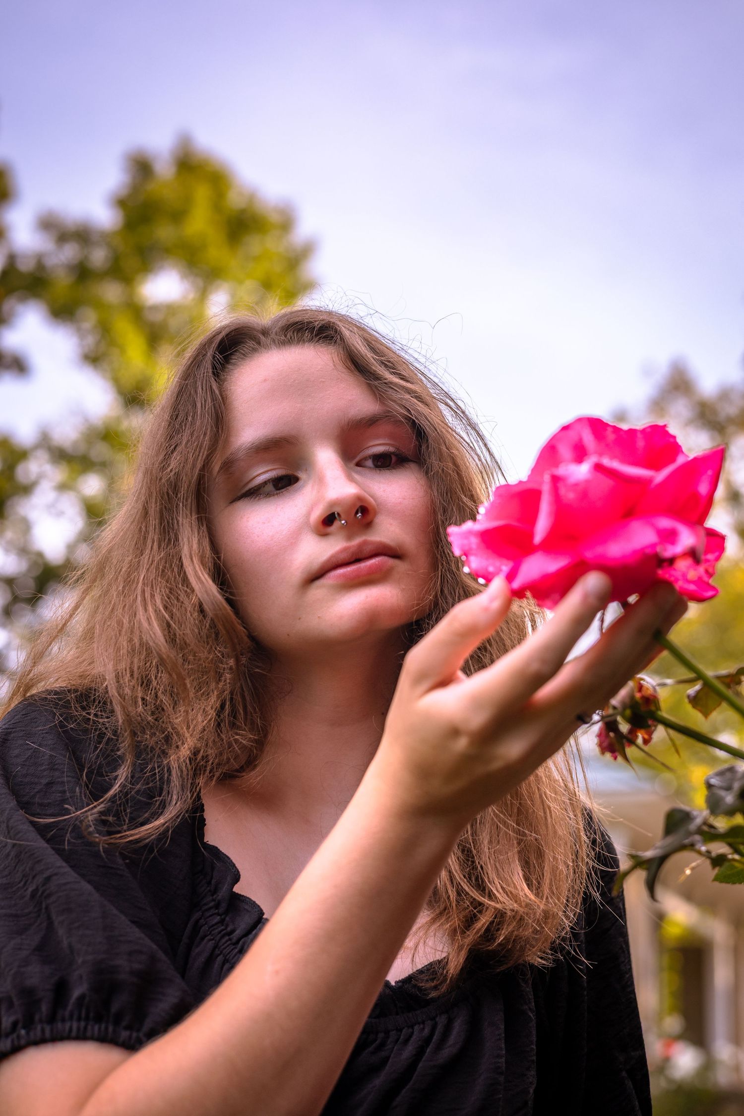 Close-up shot of someone holding a vibrant pink rose against a soft sky background.