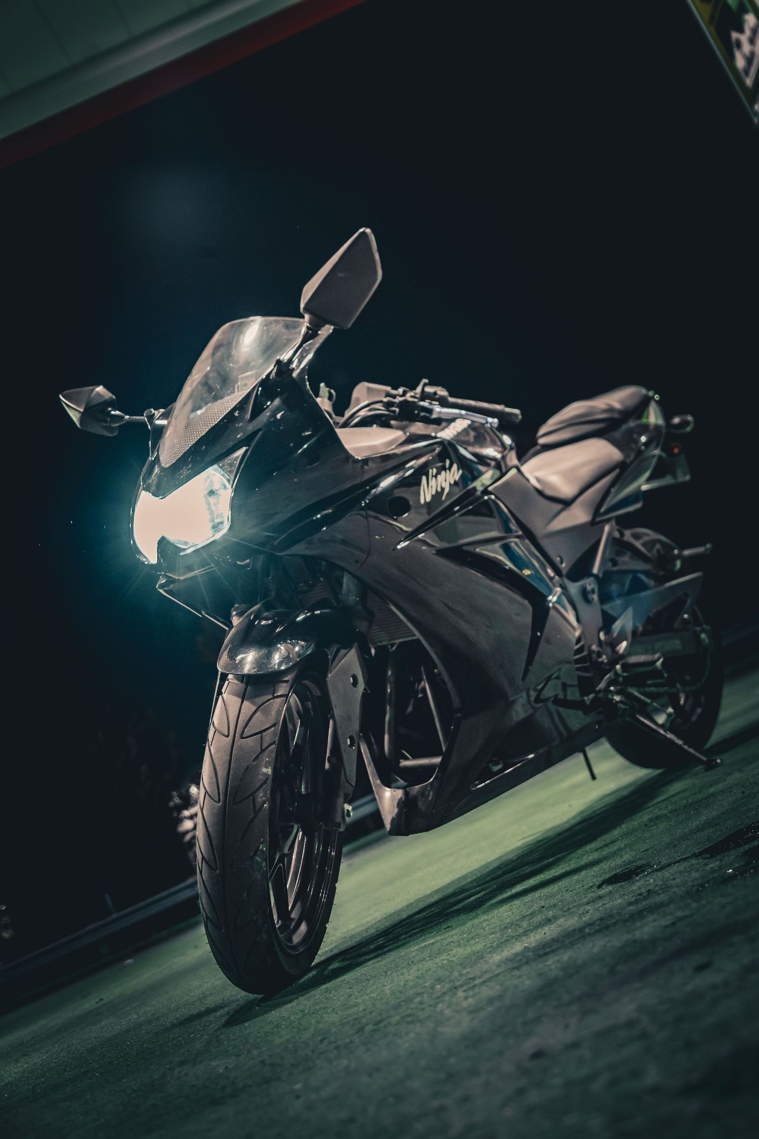 Black Kawasaki sport motorcycle with headlight on parked in a dark garage at night.