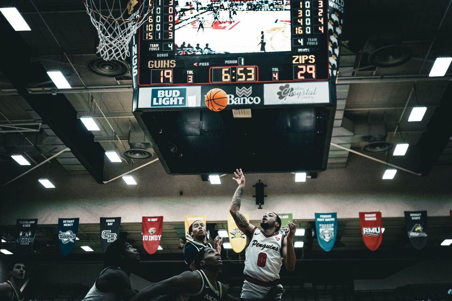 Indoor basketball court with scoreboard and overhead lighting visible.