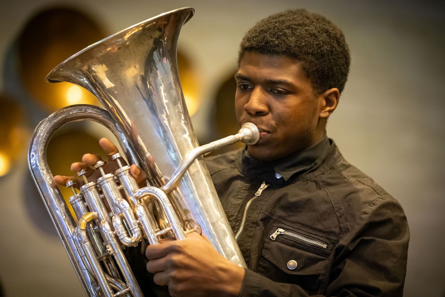 Young musician playing a silver euphonium brass instrument, focused expression, indoor performance setting.