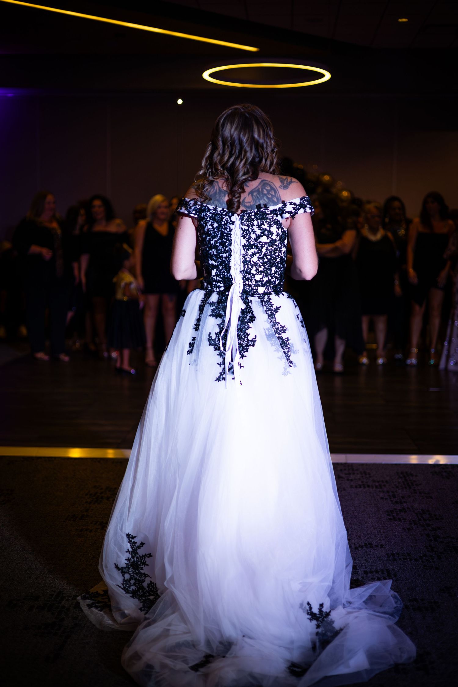 Back view of bride in white and black lace gown under dramatic lighting.