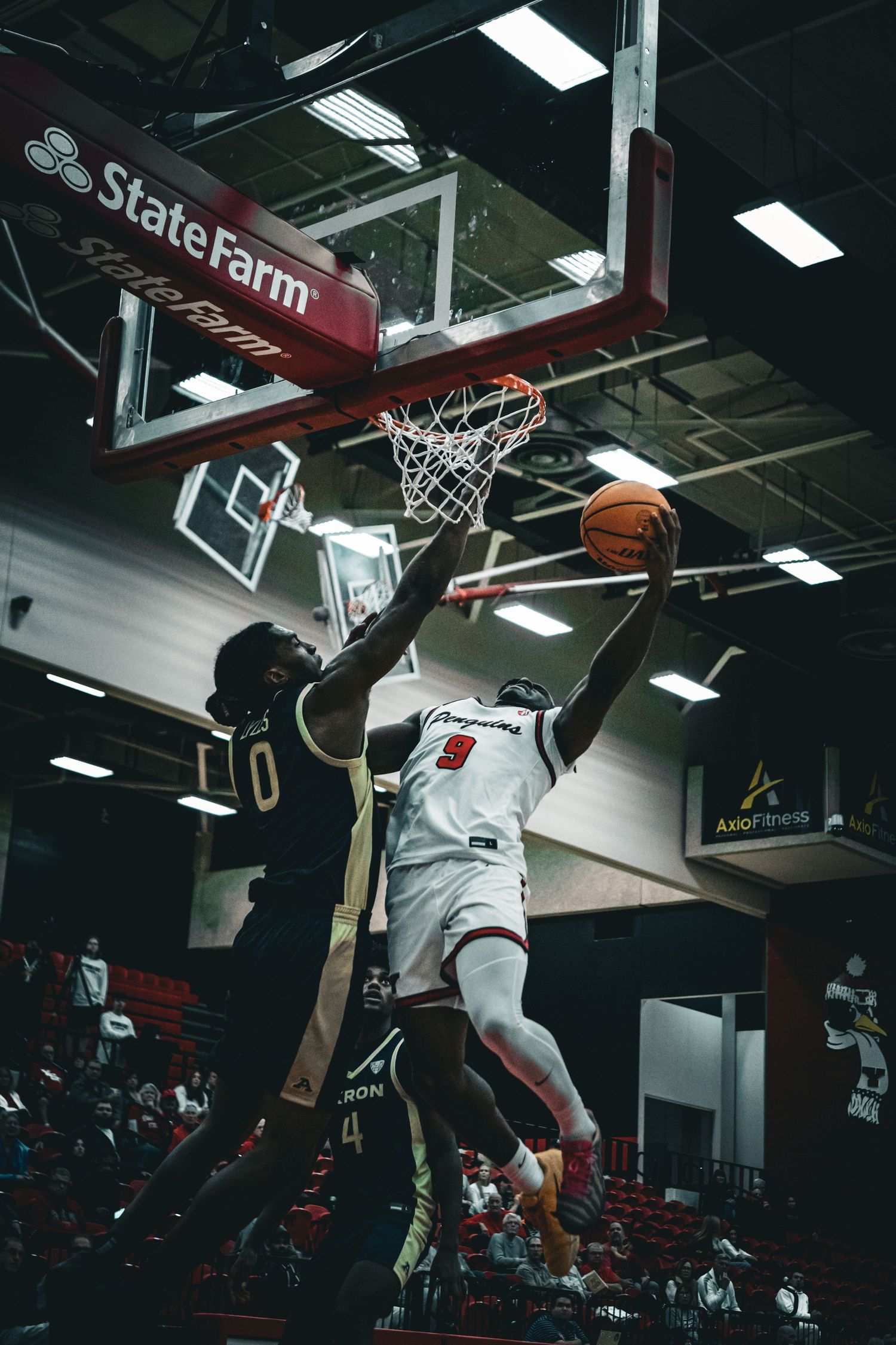 Basketball players jump for the ball near the hoop during an indoor game.