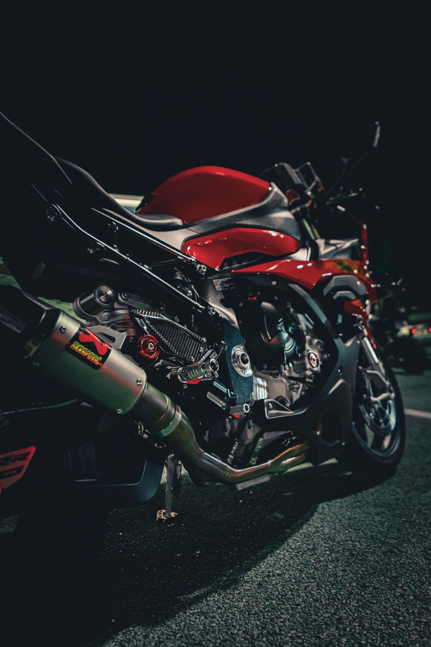 Red sport motorcycle with Akrapovic exhaust system parked outdoors at night, side detail view.