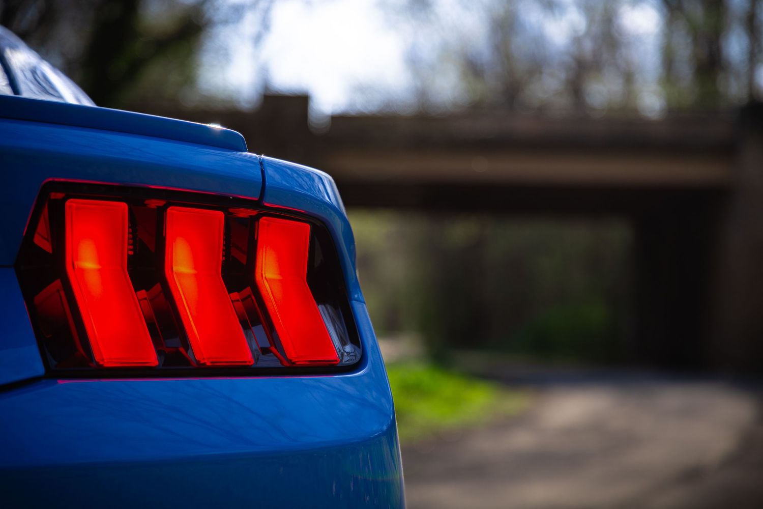 Blue sports car with glowing red tail lights parked in a wooded area at dusk.