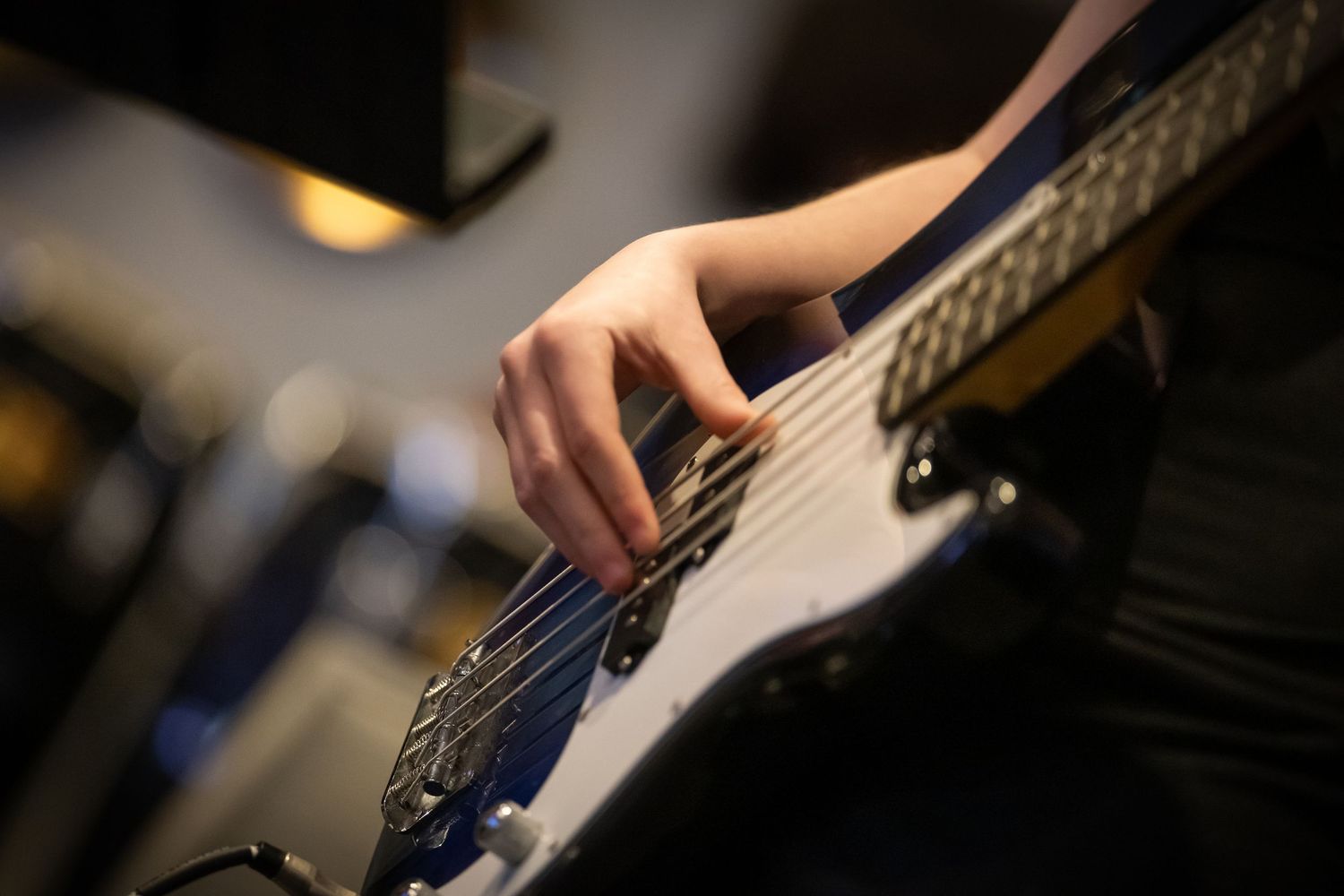 Close-up of a hand playing an electric bass guitar, fingers pressing strings on the fretboard.