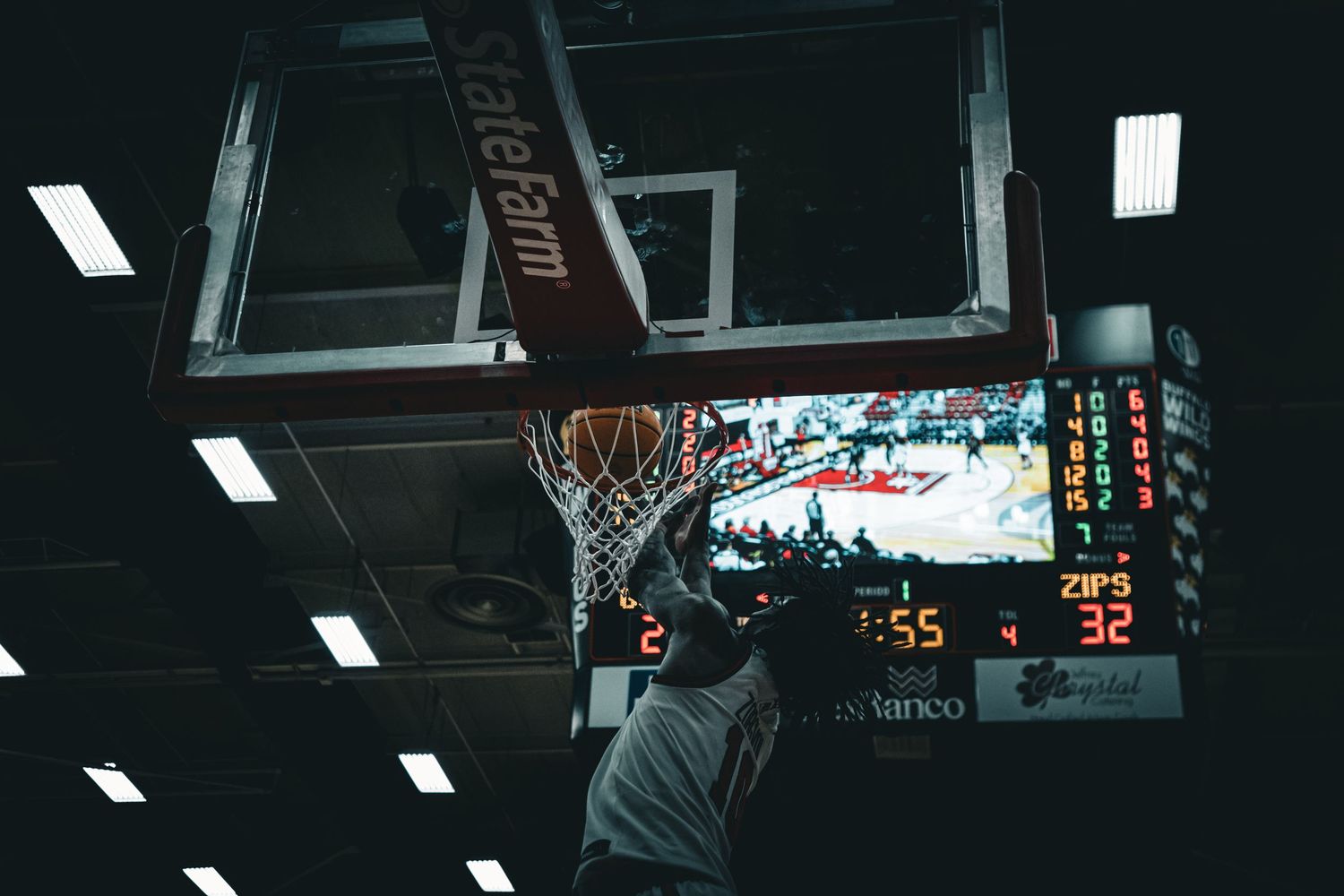 Basketball scoreboard and hoop visible in dimly lit indoor gymnasium.