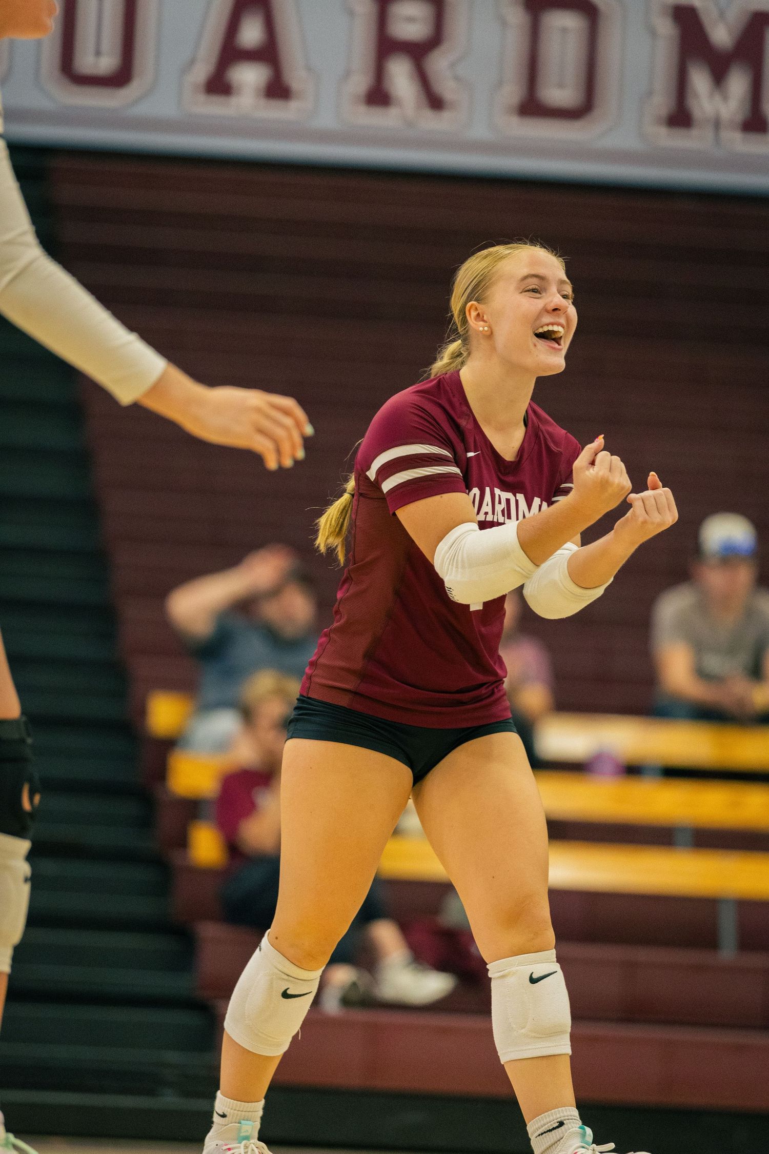 Volleyball player in maroon uniform prepares to receive ball during indoor match.