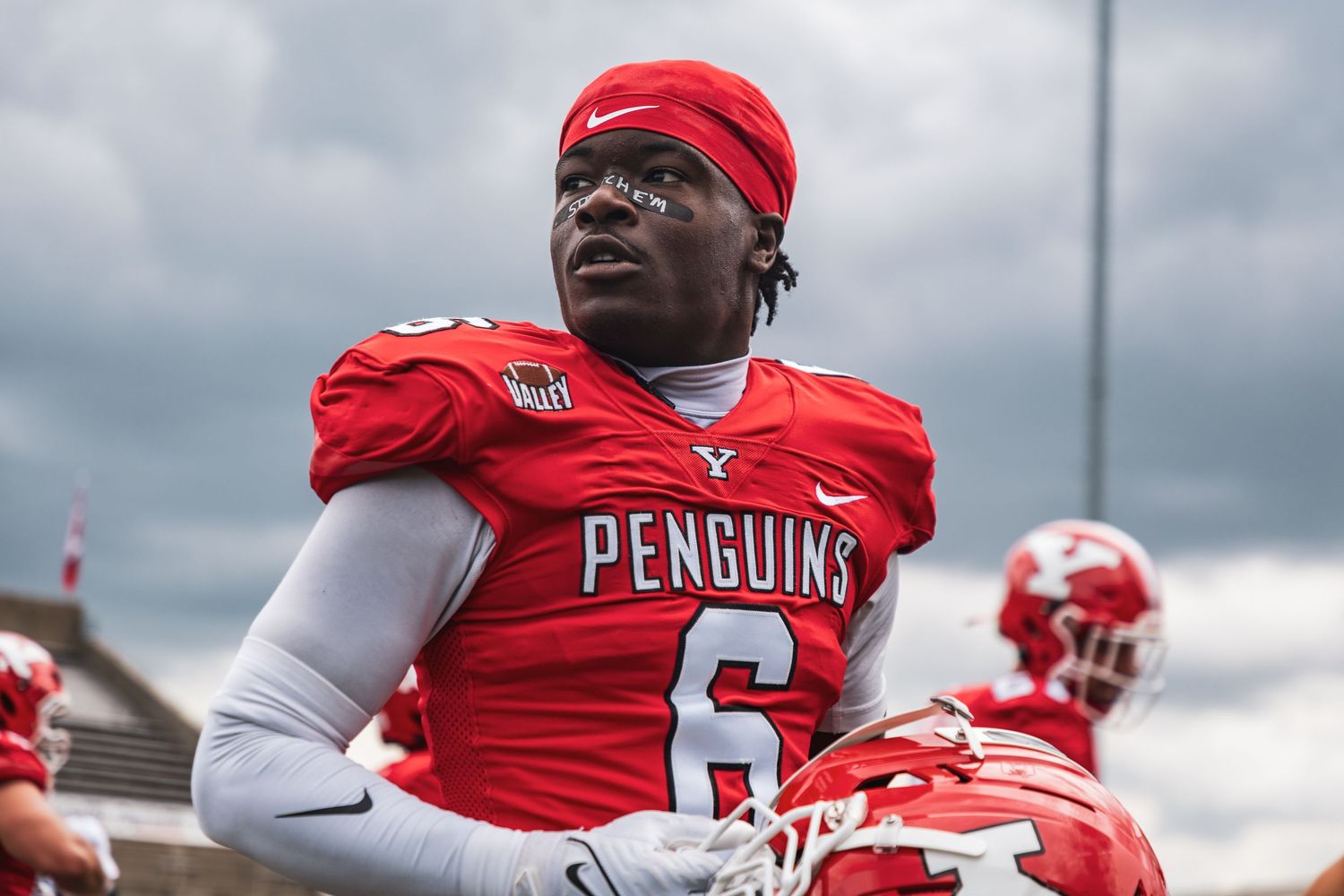 Football players in red jerseys lined up on field under cloudy skies.