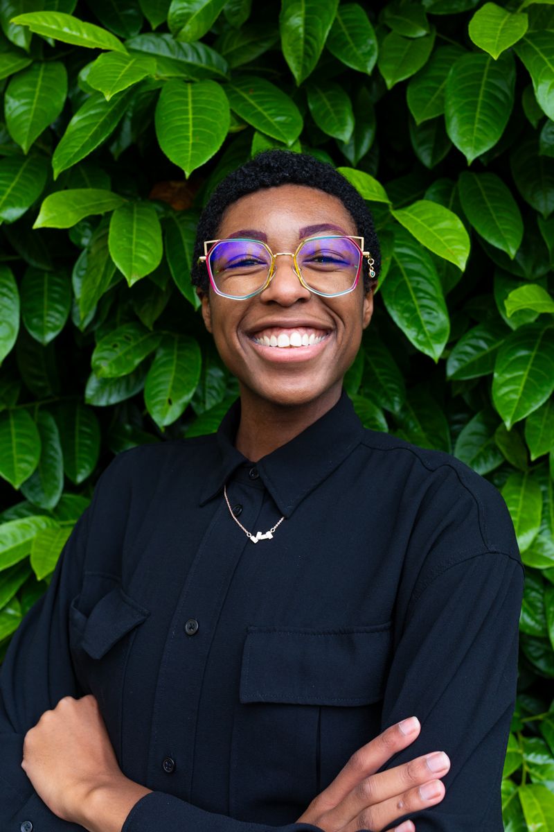 A headshot of Kassidy/KLo standing in front of greenery.