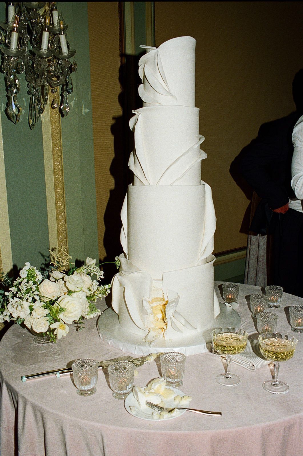 Elegant white tiered wedding cake with modern design elements displayed on a round table.