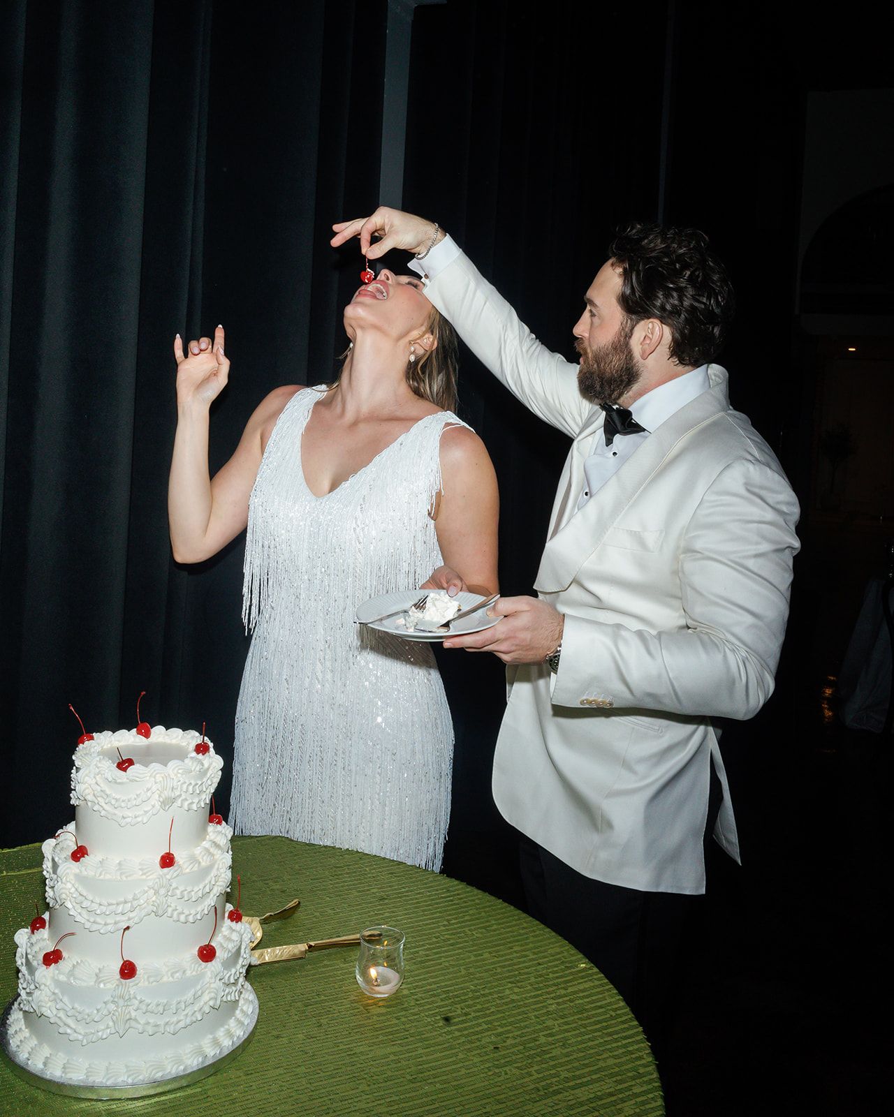 Wedding couple sharing cake cutting moment at reception with white tiered cake.