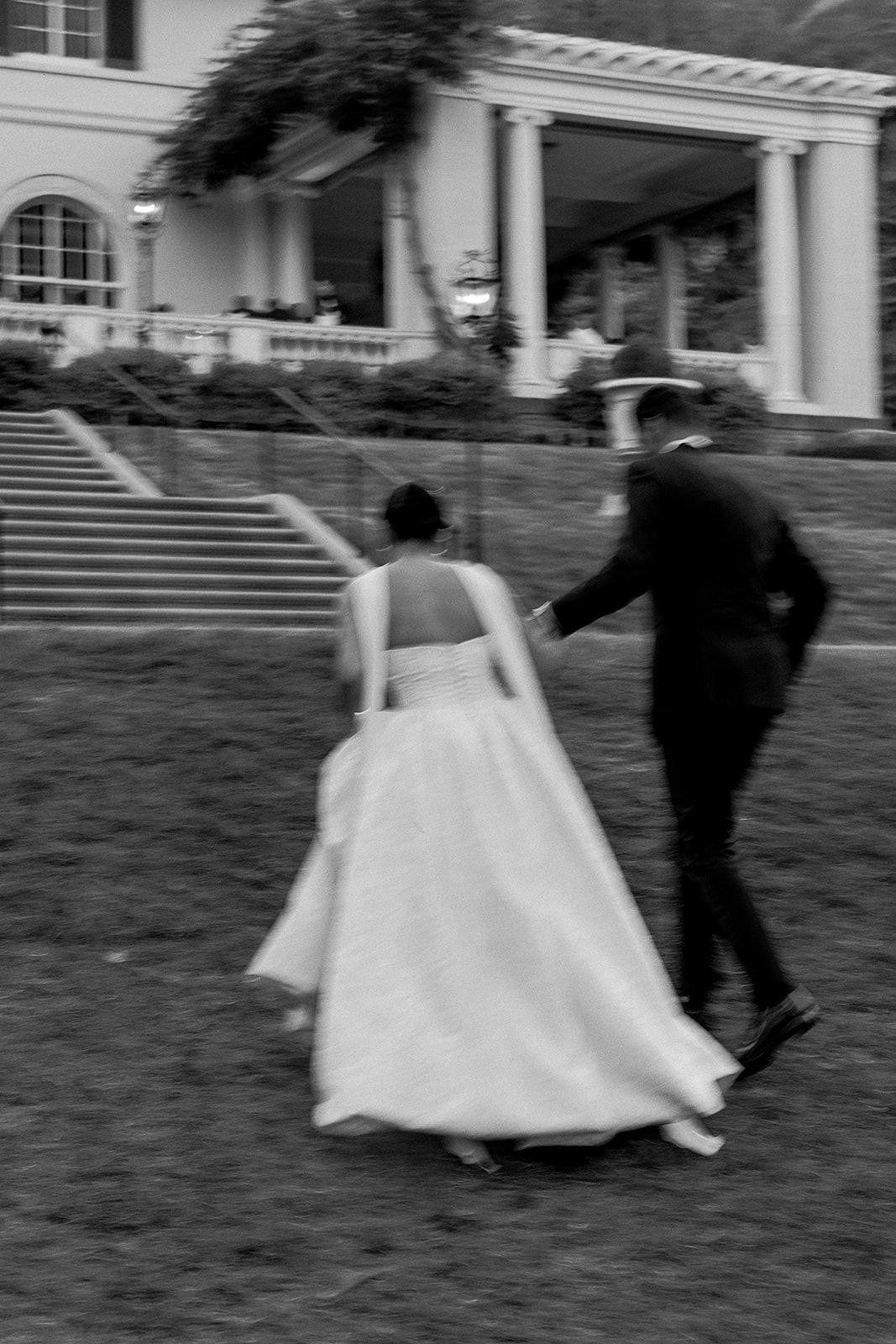 A couple dances and spins on a grassy lawn in front of a stately building.