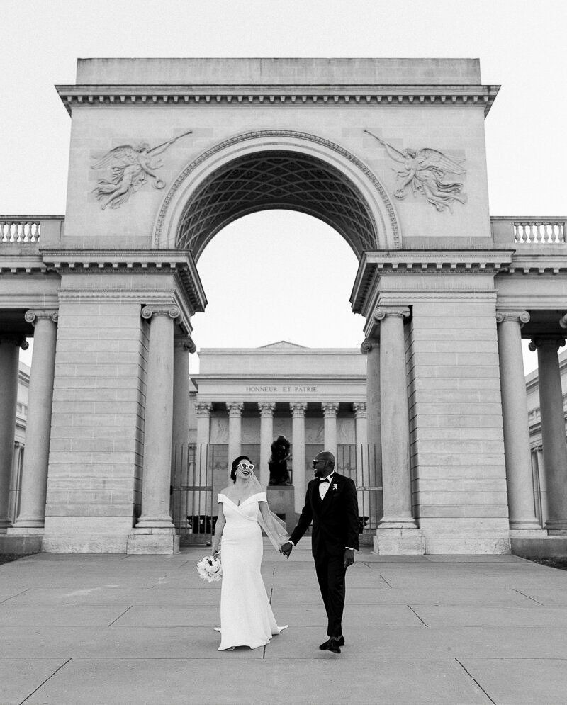 Wedding portrait photography of a coupe walking through the grand archway at Legion of Honor after their ceremony.