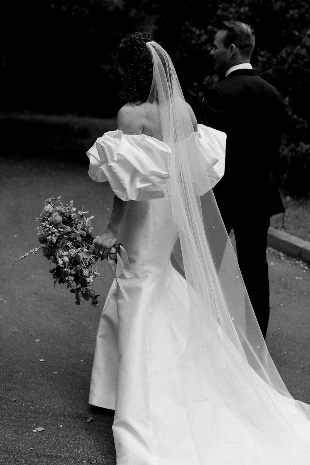 A bride in an elegant white dress holds a bouquet while standing next to her groom.