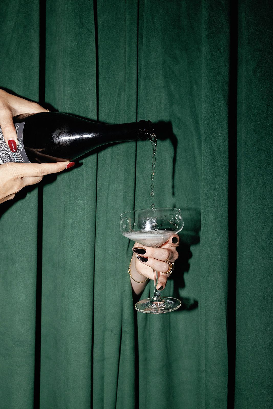 Champagne being poured into elegant glasses against a dark green wooden backdrop.
