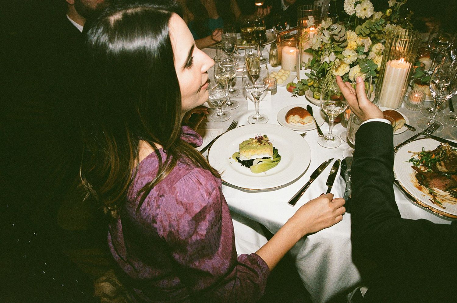 A guest enjoys dinner at an elegantly set wedding reception table with candles and fine china.