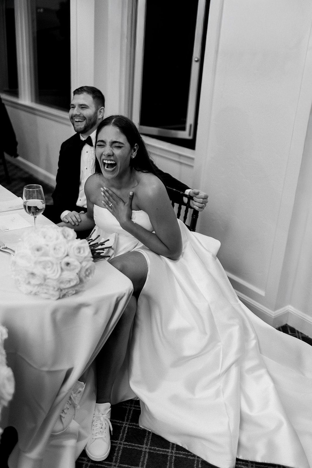 A joyful moment captured during a wedding reception with laughter at a formal dinner table.