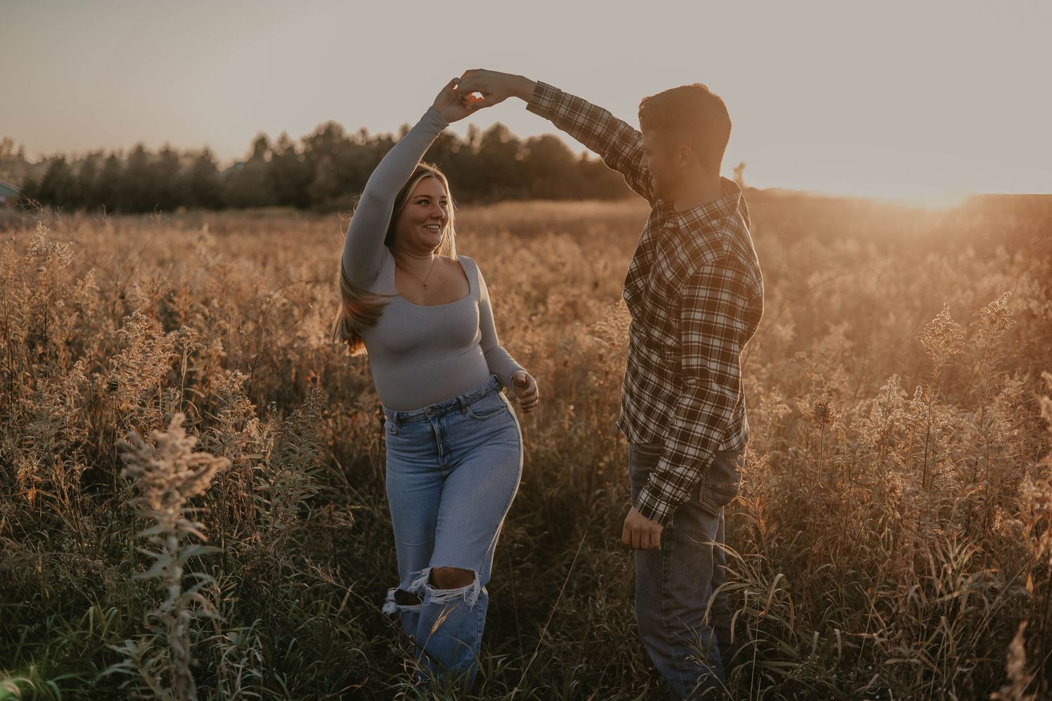 A couple dances together in a golden sunlit field during sunset on a warm evening.