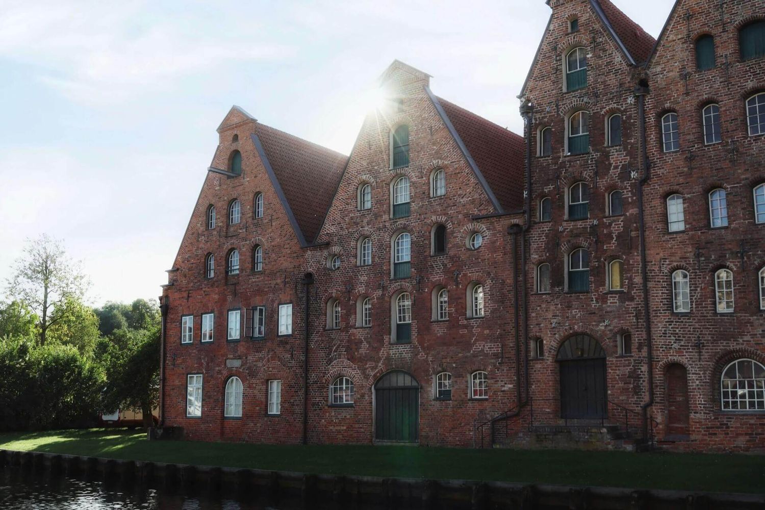 Historische Lagerhäuser aus rotem Backstein spiegeln sich im ruhigen Wasser entlang einer traditionellen deutschen Uferpromenade.