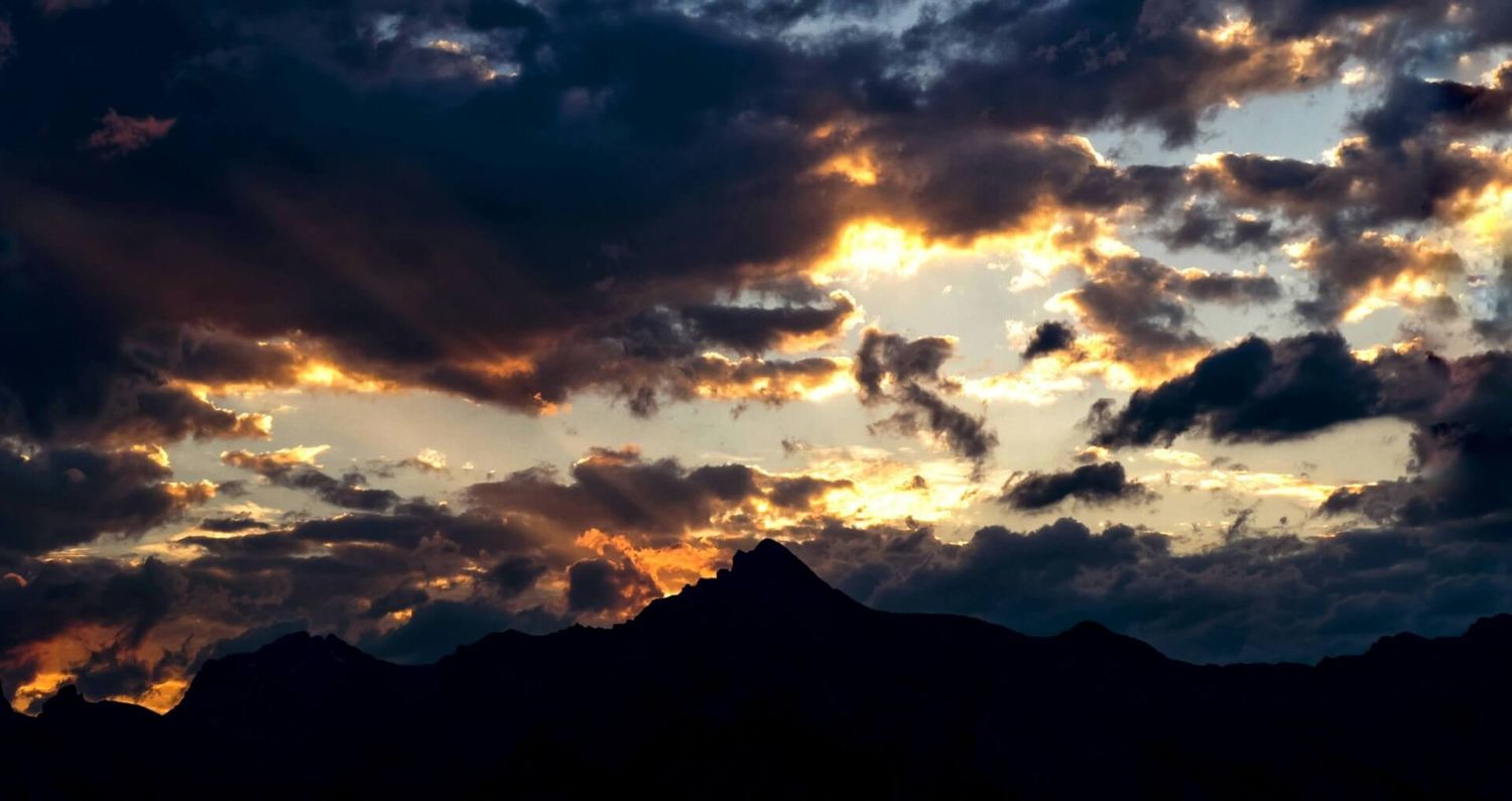 Dramatische dunkle Wolken, durch die das Sonnenlicht bricht, schaffen eine stimmungsvolle Szene eines Sonnenuntergangs in den Bergen.