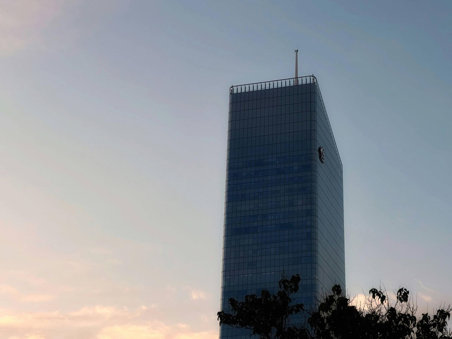 Moderner gläserner Wolkenkratzerturm vor einem Sonnenuntergangshimmel mit warmen Farbtönen.