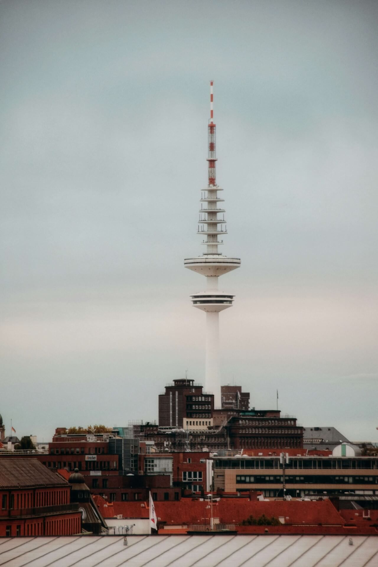 Der Heinrich-Hertz-Turm in Hamburg erhebt sich über roten Dächern gegen den wolkenverhangenen Himmel mit drückender Sonne.