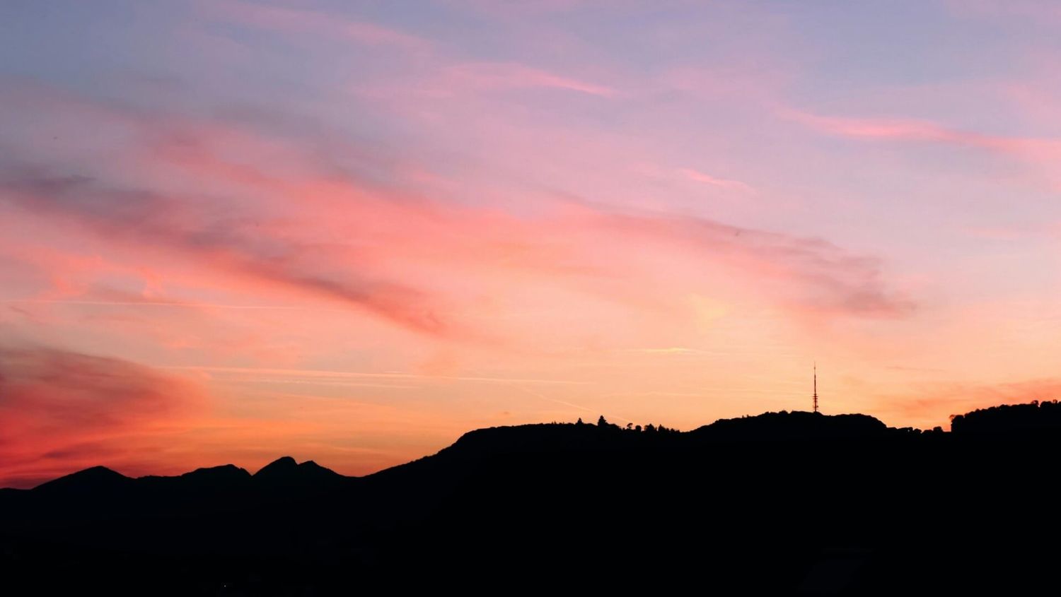 Der rosafarbene und lilafarbene Himmel bei Sonnenuntergang zeichnet die Silhouette der Gebirgskämme am Horizont.