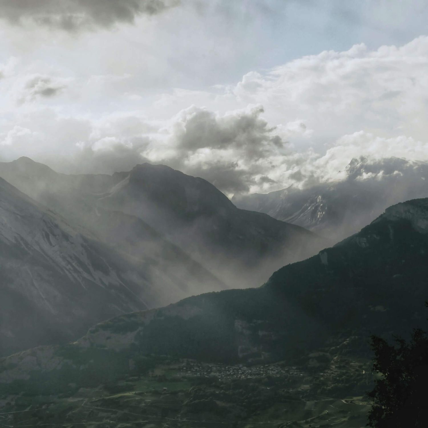 Grandiose Berglandschaft, eingehüllt in Wolken und Nebel, durch die die Sonnenstrahlen scheinen und eine stimmungsvolle Atmosphäre schaffen.