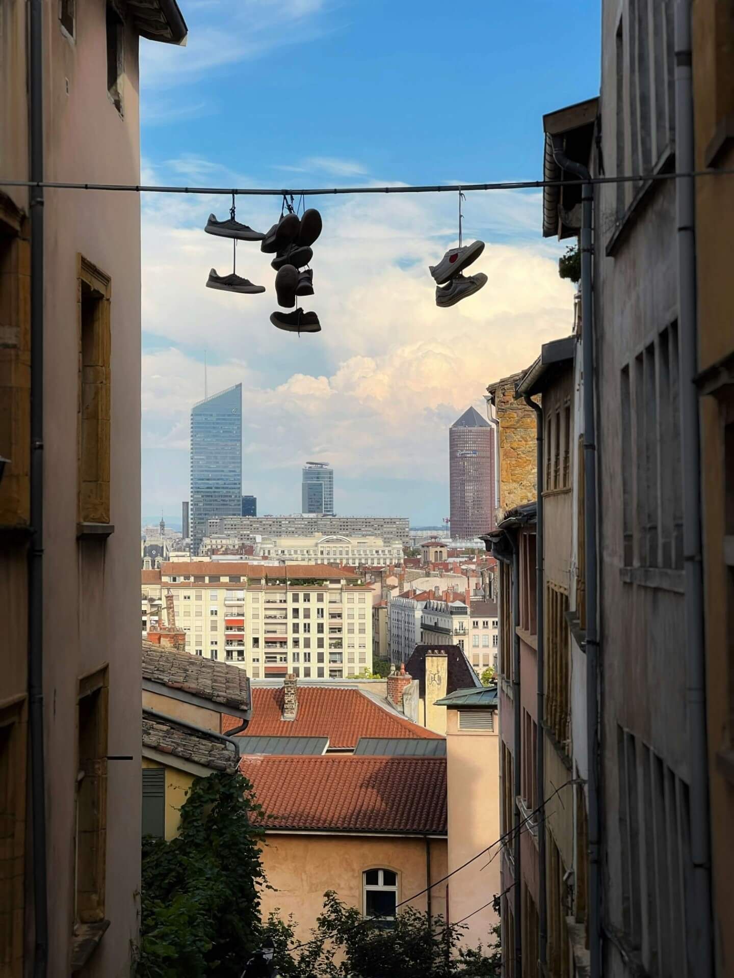 Hängende Turnschuhe an einer Telefonleitung umrahmen die moderne Stadtsilhouette von Lyon mit Wolkenkratzern im Hintergrund.