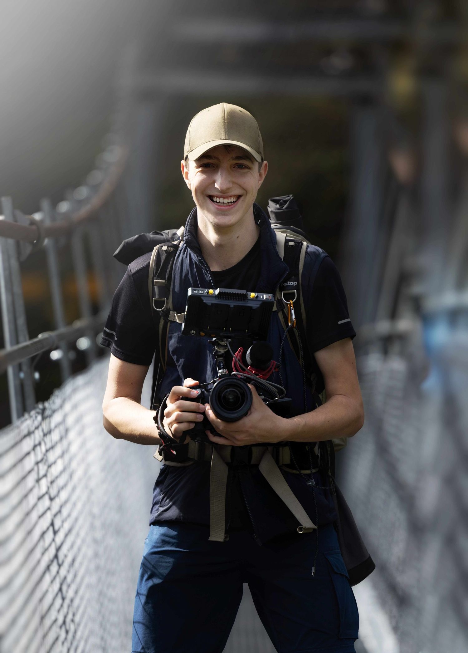 Ein Fotograf steht auf einer Brücke mit professioneller Kameraausrüstung und lacht entgegen.