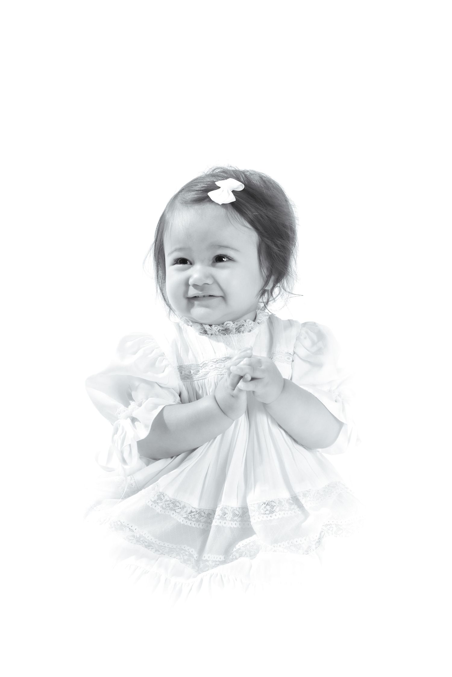 Black and white portrait of a smiling baby girl in a white lace dress with a bow in her hair.