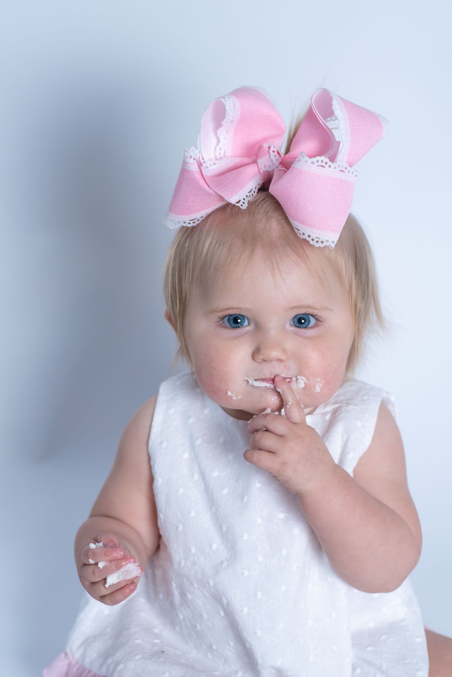 Sweet baby in white dress wearing large pink bow accessory with lace trim.