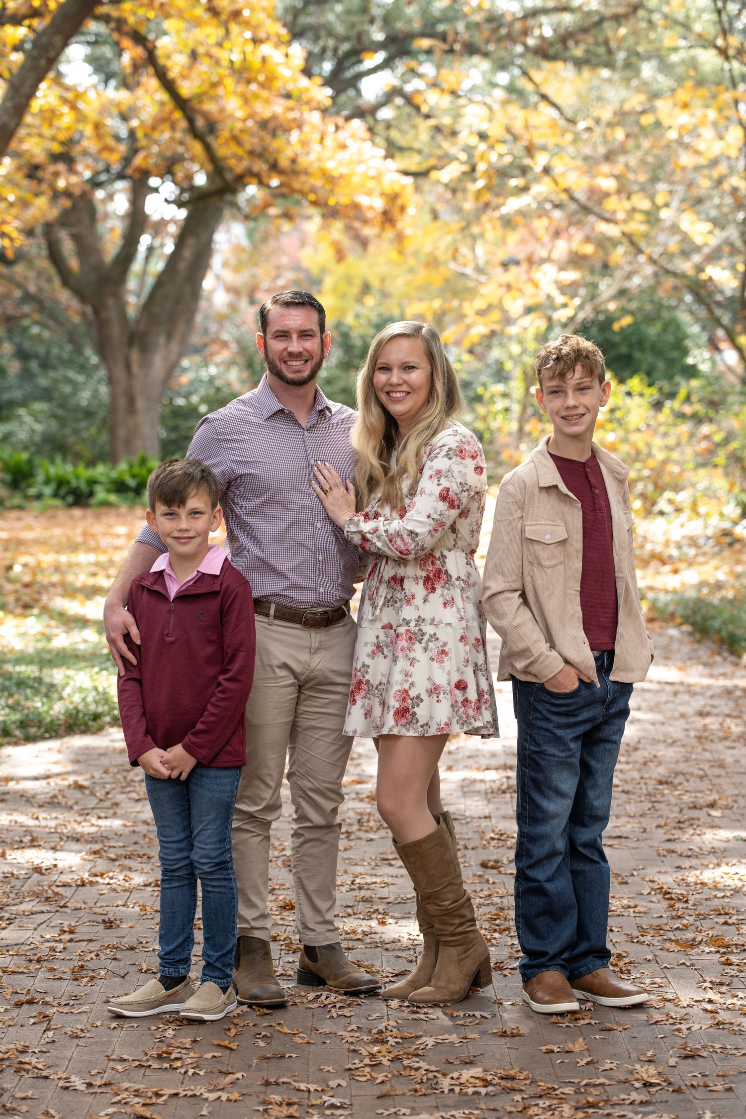 Family of four poses outdoors among autumn foliage, wearing coordinated outfits in maroon and neutral tones.