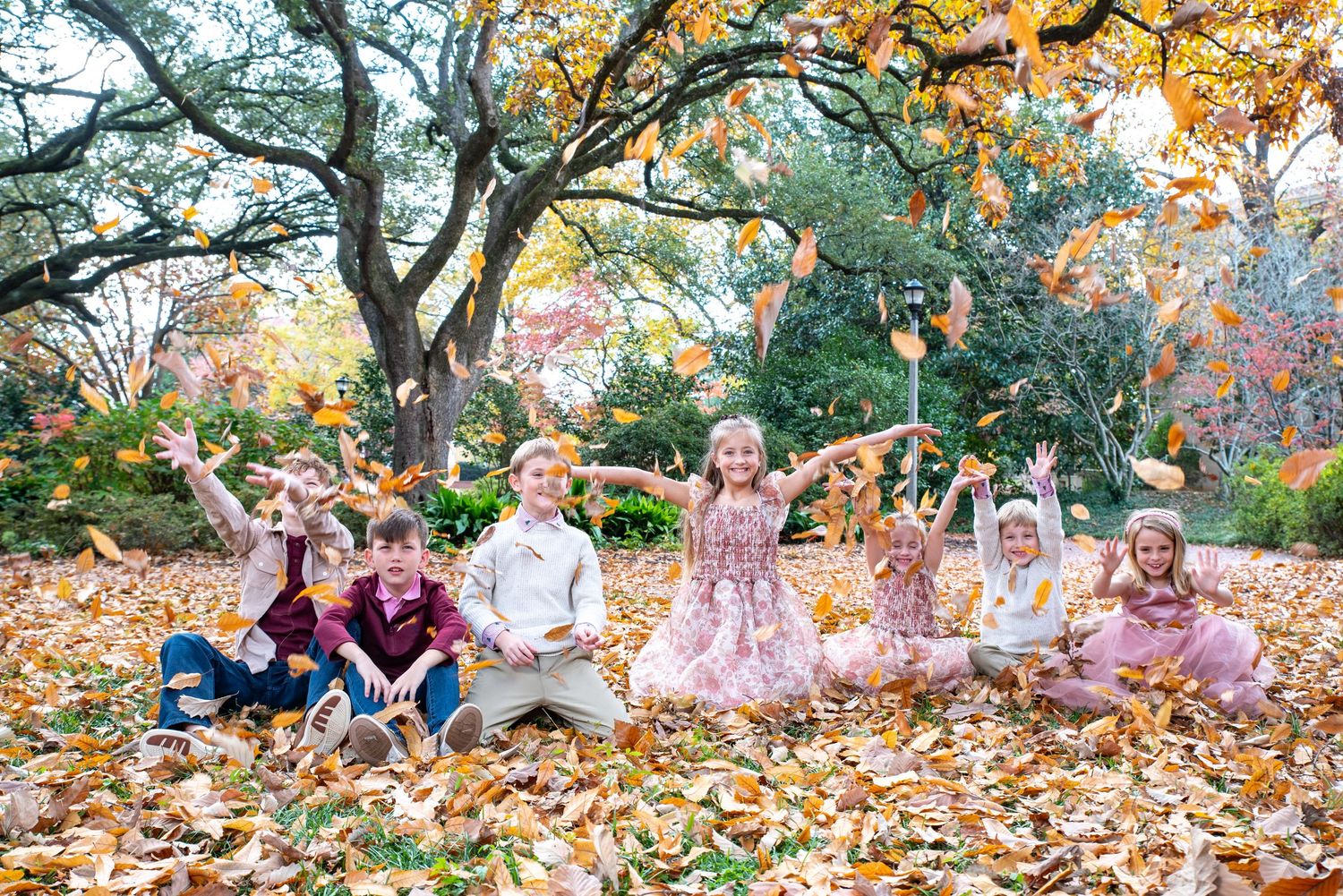 Children tossing autumn leaves in a colorful fall park setting, laughing and playing together outdoors.