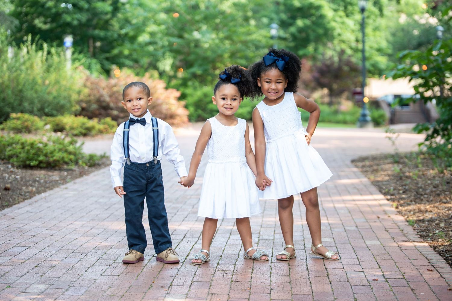 Three children in formal attire holding hands on brick pathway at USC Horseshoe in Columbia, SC.