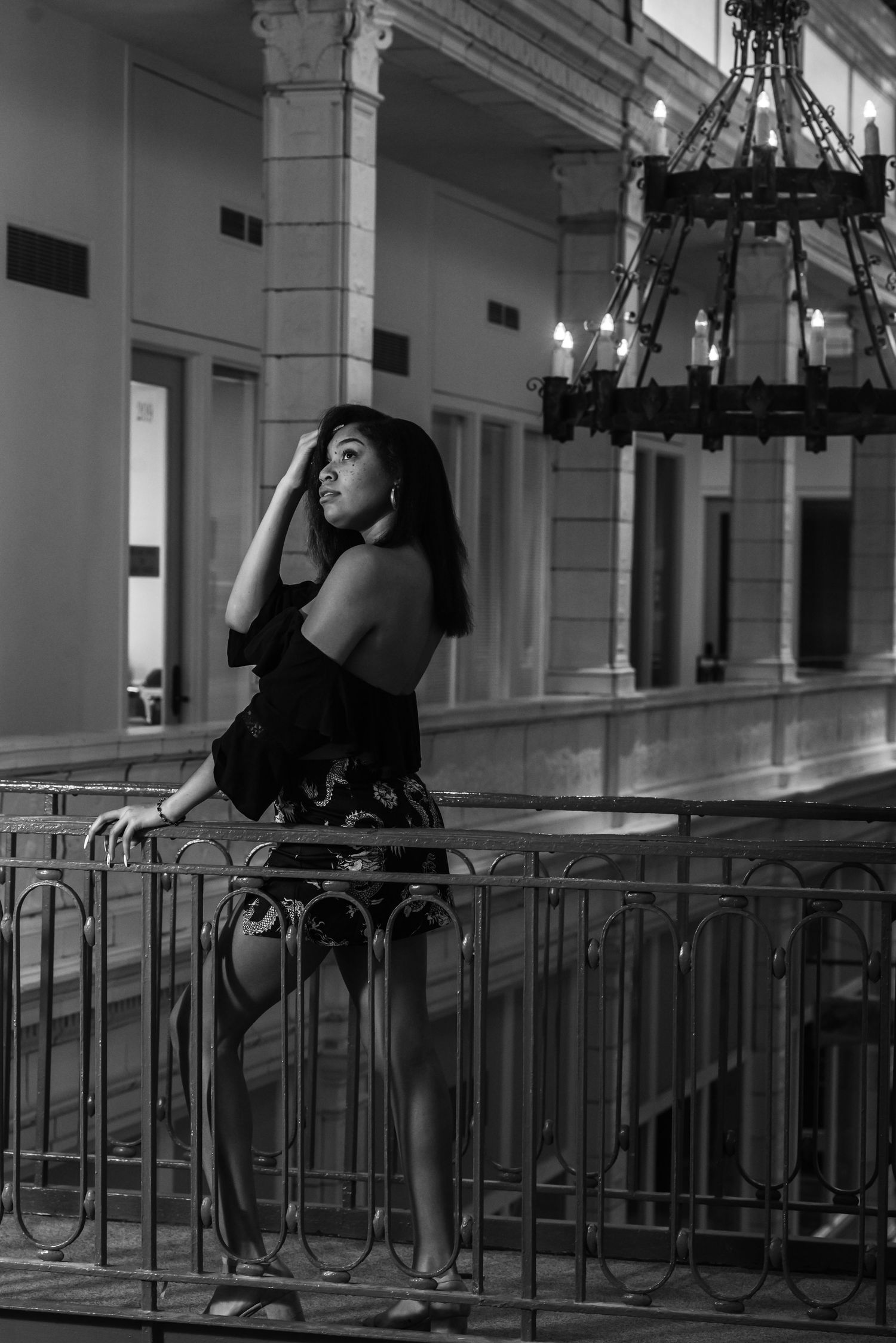Artistic black and white portrait of woman in formal dress posing by ornate railing.