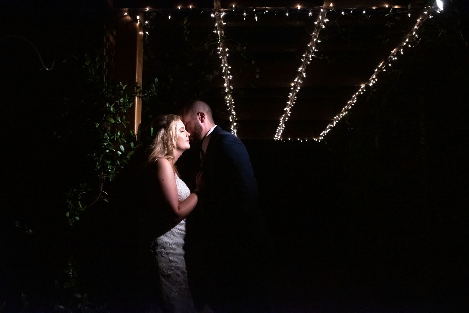 Romantic nighttime wedding photo with couple silhouetted against twinkling string lights.