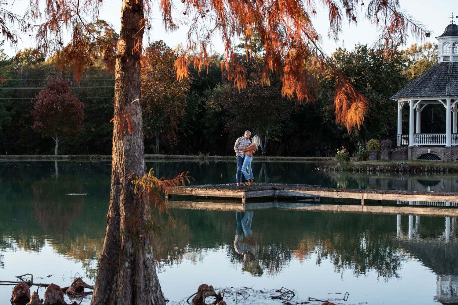 Couple standing on dock over reflective lake at sunset at Bock Estate & Venue in Camden, SC..