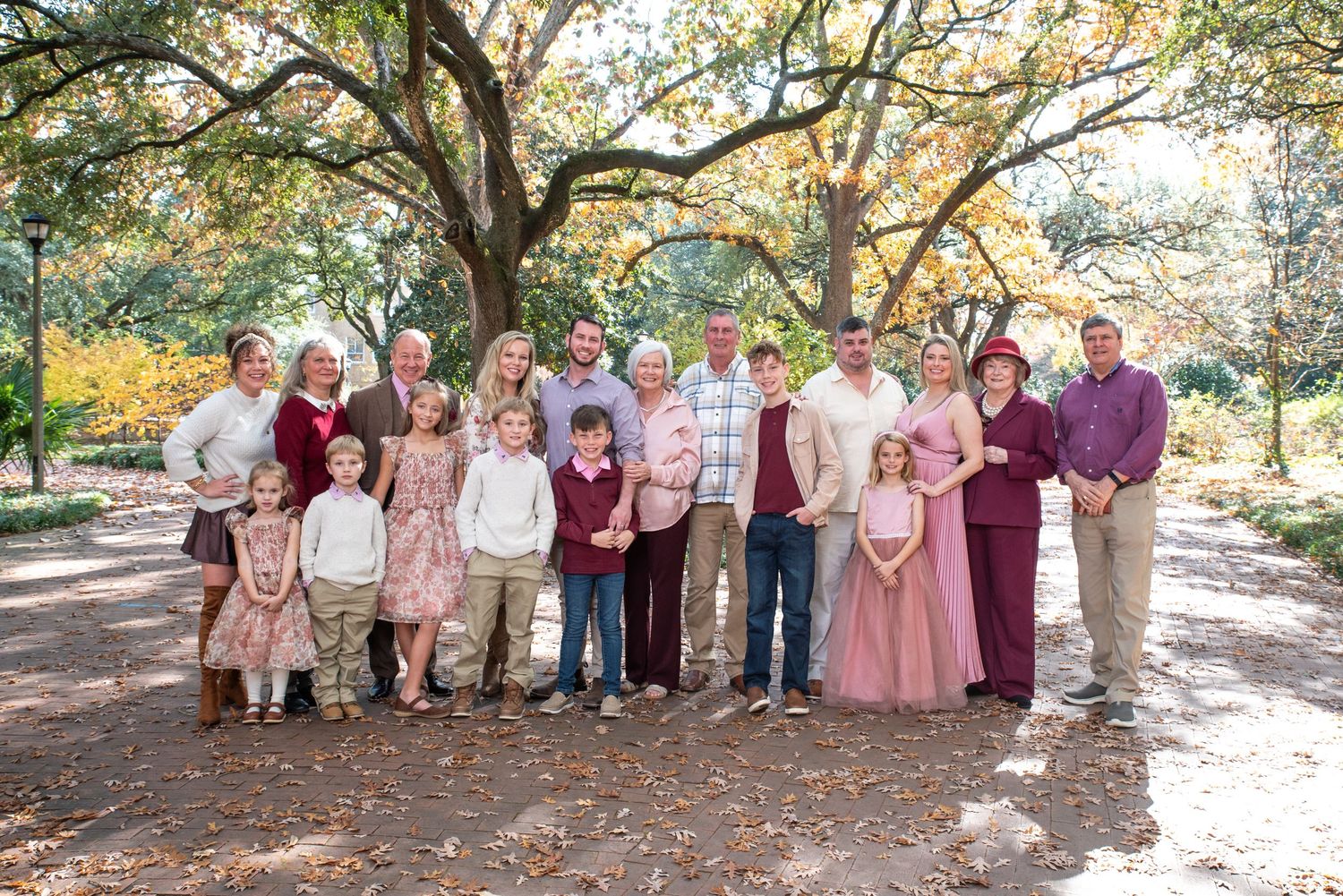 Large family group portrait outdoors under oak trees, dressed in coordinating neutral and mauve tones for a fall photo session.