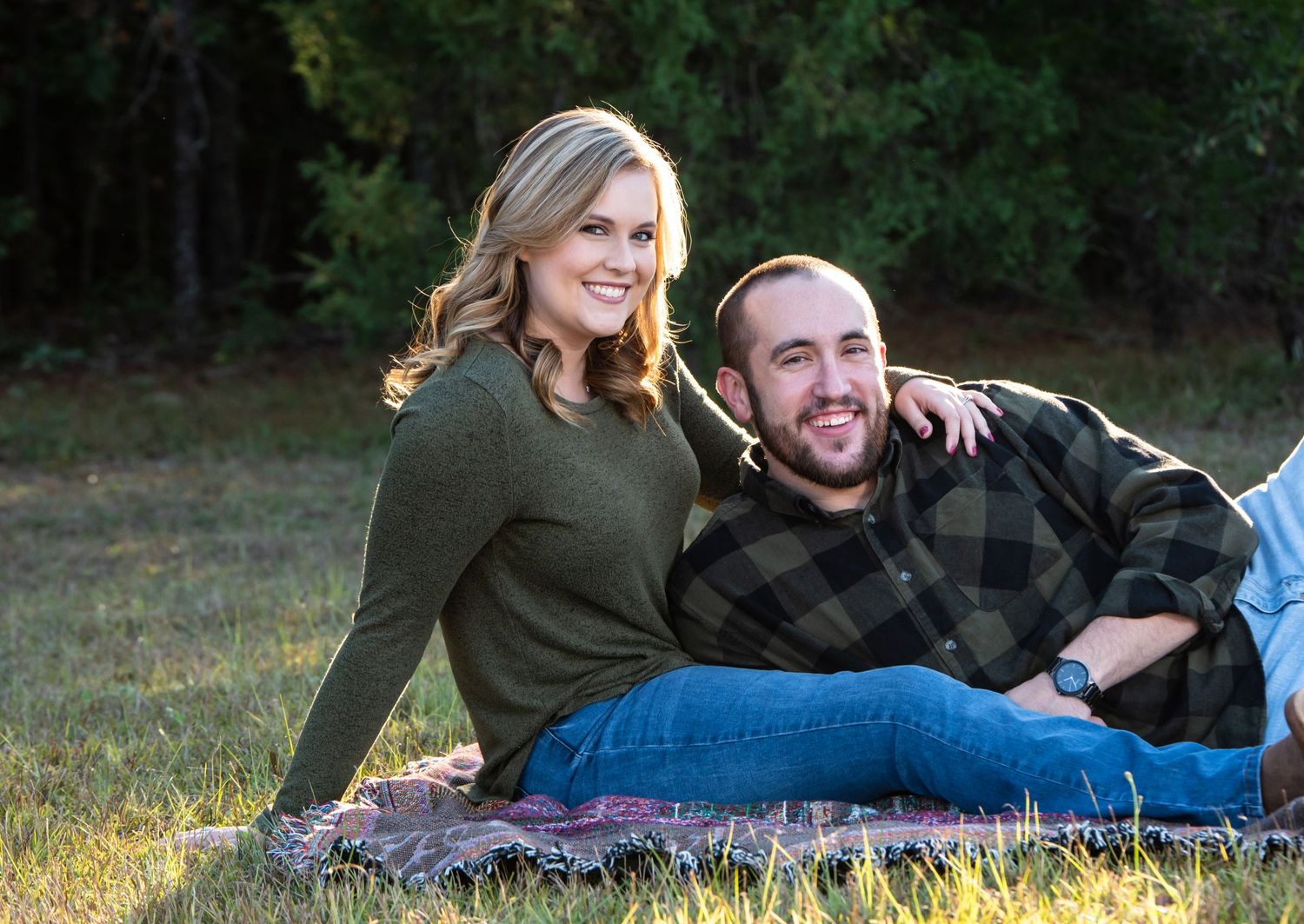 A couple relaxes together on a blanket in a grassy field at sunset.