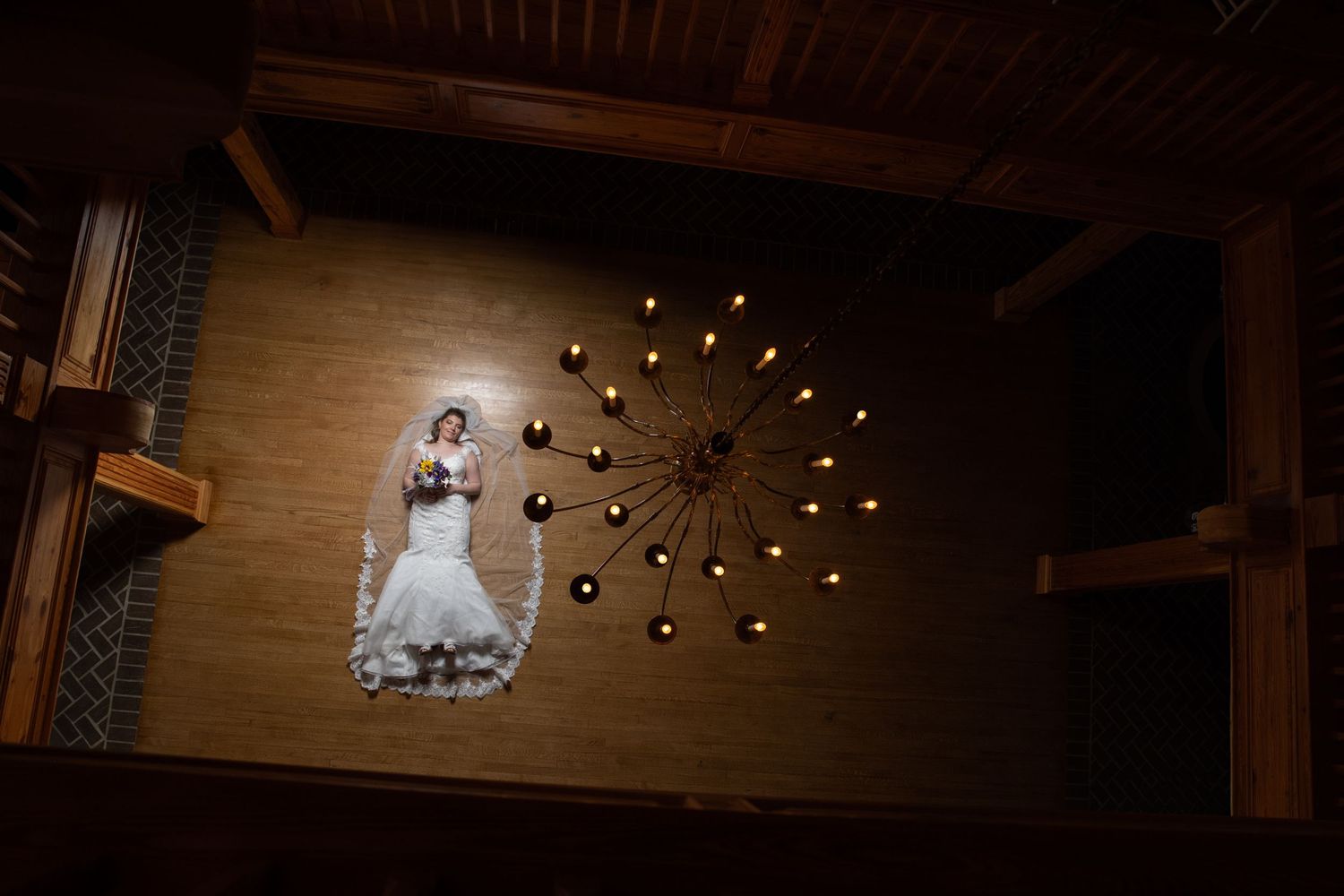 A white wedding dress laid flat on wood flooring with multiple lightbulbs arranged in a sunburst pattern above it.