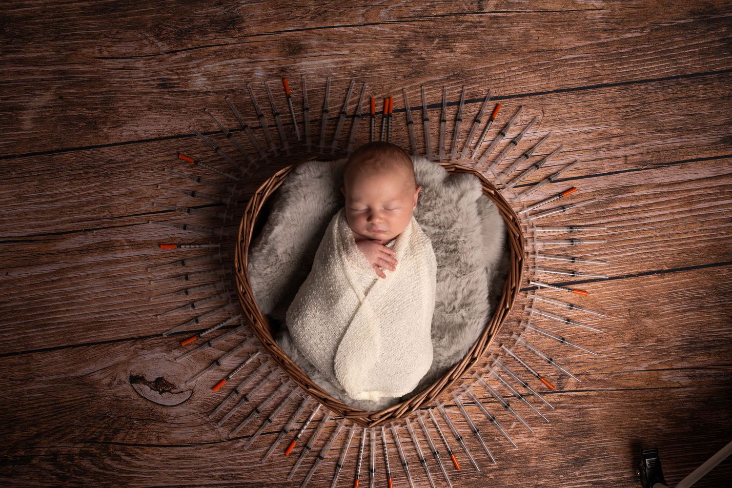Newborn baby swaddled in white wrap sleeping peacefully in a heart-shaped wicker basket on rustic wood floor.