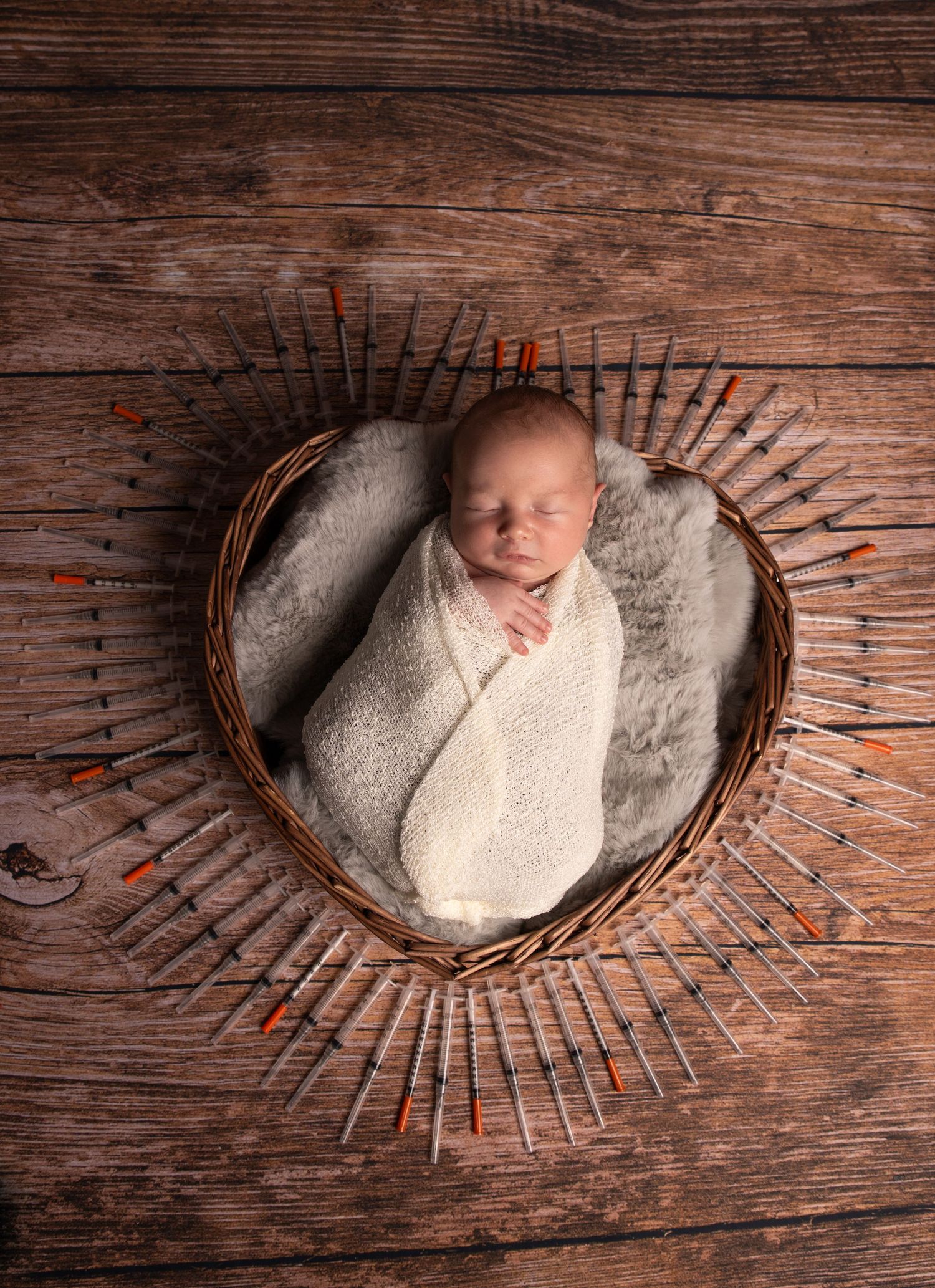 Newborn baby swaddled in white wrap sleeping peacefully in a heart-shaped wicker basket on rustic wood.