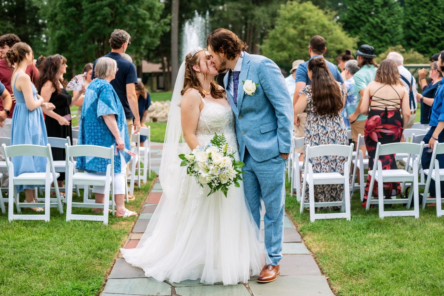 Outdoor garden wedding ceremony with blue and white decor and natural greenery.