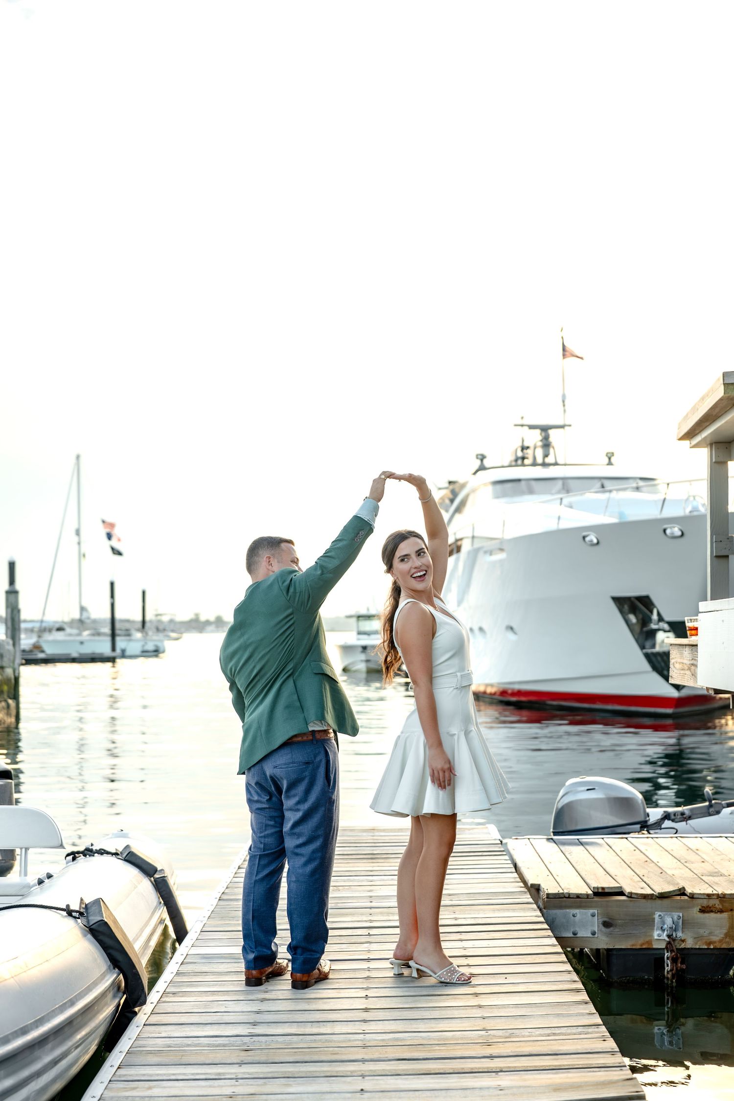 Couple dancing on a marina dock with luxury yachts in the background at sunset.